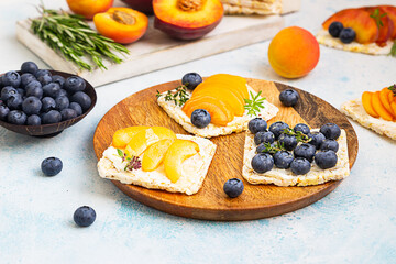 Mini rice cakes with blueberries, apricots, nectarines and cream cheese with honey for healthy breakfast. Light blue background. Summer dieting sandwiches.