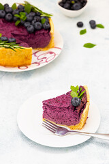 Piece of blueberry or bilberry cheesecake decorated with fresh berries, mint and rosemary. Light concrete background. Selective focus.