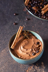 Coffee and chocolate pudding or mousse in a ceramic bowl with cinnamon and anise star, selective focus. Dark brown concrete background.