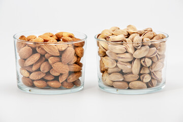 Pile of salted pistachios and almonds in glass bowl on white background.
