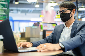 Asian businessmen are talking on the phone and using note book for working ,he wearing mask for protect coronavirus