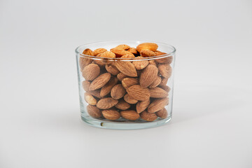 Pile of almonds in glass bowl on white background.
