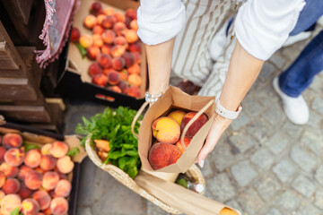 Unrecognizable woman hands holding paper bag with organic peaches outdoors at farmers market.