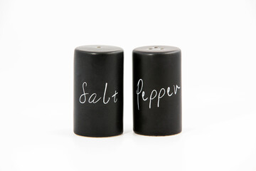 Black porcelain salt and pepper shakers on the white background with some salt and copy space. Simple and elegant, minimalist design.
