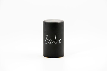 Black porcelain salt shakers on the white background with some salt and copy space. Simple and elegant, minimalist design.