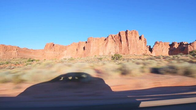 Pov point of view panning driving vehicle side view shot on arches scenic drive at Arches National Park in Moab, Utah at sunrise with canyons rock formations and car shadow on road trip