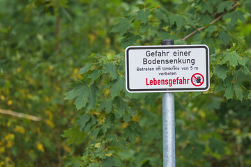 Ein Warnschild in einer Tagebaufolgelandschaft mit der Aufschrift Gefahr einer Bodensenkung  ,...