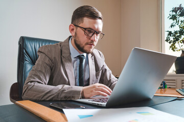 Young businessman in glasses working on a laptop in his personal office.