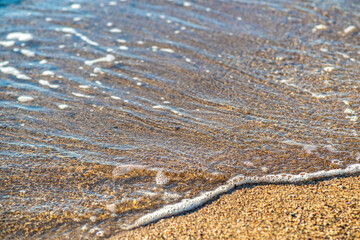 Close up of small sea waves with clear blue water over yellow sand beach at summer sunny shore.