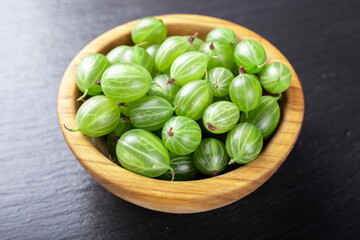 Fresh gooseberries in wooden bowl on black stone slate background.