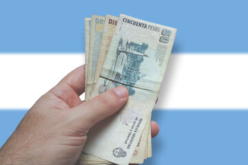 Man's hand holding Argentine money. Banknote Argentine money. Isolated on background with blurred Argentine flag. Finance concept.
