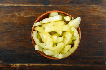 Sliced raw yellow peppers in a bowl on a wooden background. Vegetable, ingredient and staple food.