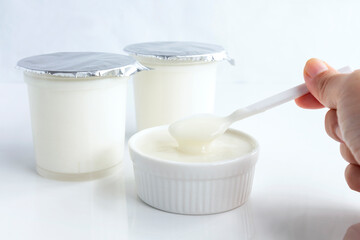 Healthy flavored yogurt on spoon in the woman hand holding and in ceramic bowl with package plastic cup on white background. with copy space for your text.