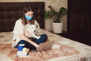 Young woman in protective mask with pet works, studies at laptop at home. Working from home. Concept home quarantine, prevention COVID-19, Coronavirus outbreak situation.