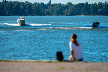 An alone female sitting on the waterfront watching the sea and passing by leisure boats.