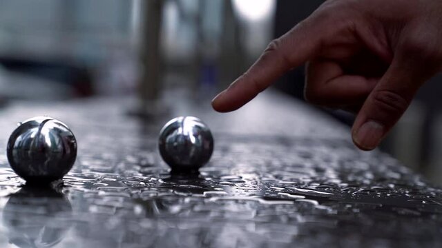 A close-up of a man hand rolling two mirror-reflecting balls over a wet surface, then taking them in his hand