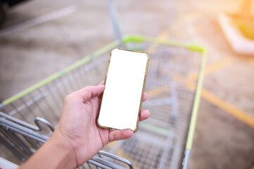 Holding a smartphone white screen with blurred shopping cart background.