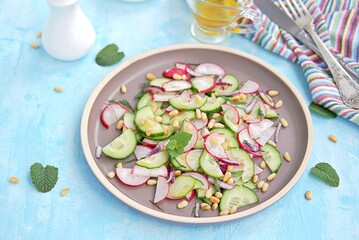 Light salad of crispy radish, cucumber and mint leaves with citrus dressing on a brown plate.