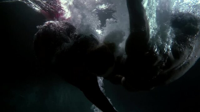 Close-up of a dark underwater depth and a man and a woman fall into it from the surface, Around them darkness and bubbles