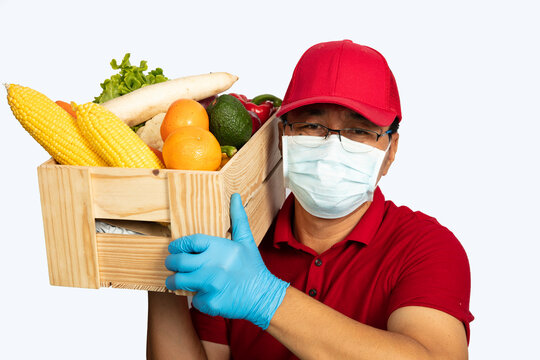 Delivery man with red uniform and face mask carry wooden box contain vegetable delivery to customer at home