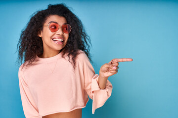 A positive cheerful curly Afro-american woman points her finger to the side.