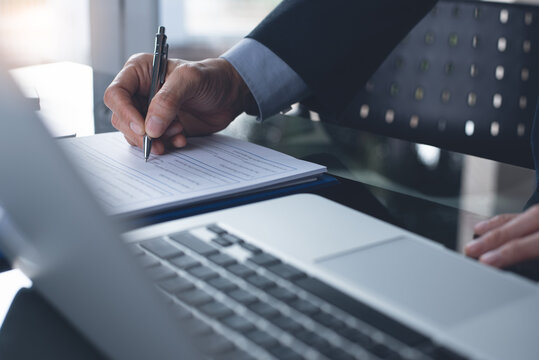 Businessman signing business contract or approval document with laptop computer on table in office