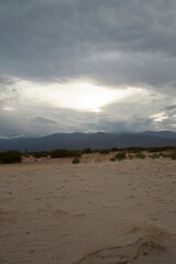 Vertical photo. Arid desert landscape at sunset. View of the sand and mountains under a dramatic cloudy sky at dusk. 