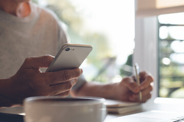 Man using mobile phone while online working on laptop computer at home office