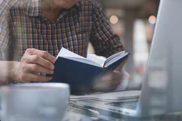 casual man reading book and working on laptop computer in coffee shop