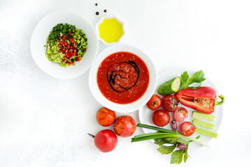 Ripe, bright vegetables-ingredients and cold gazpacho soup in a white Cup, on a white worn background. vegan and vegetarian food.