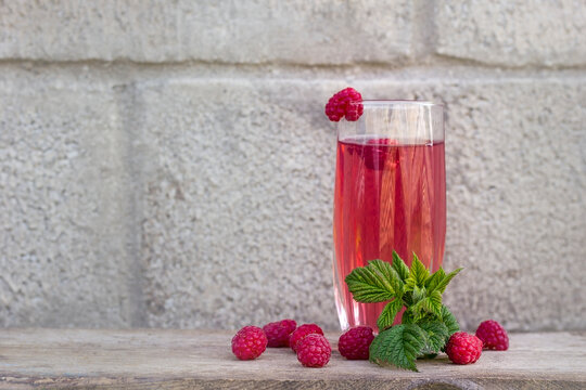 raspberry drink on a gray stone background, walls, glass cup with compote, fresh raspberries on a wooden table, cooling drink