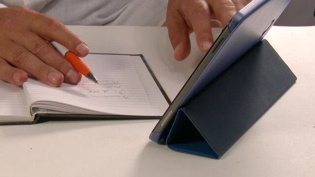 4k 50fps Man consults a tablet by sliding his fingers on the glass and taking notes on an agenda