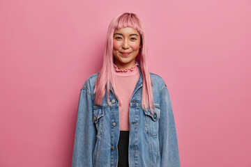 Good looking happy girl with long rosy hair, expresses positive attitude, wears long sleeved denim...