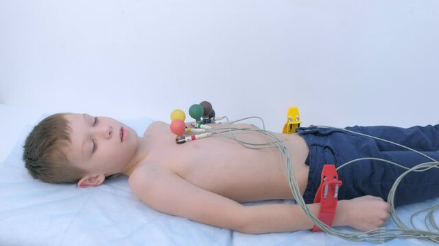 Doctor cardiologist preparing child boy to cardiogram heart procedure, side view. Woman cardiologist making heart cardiogram for child boy lying on couch putting sensors on chest, hands closeup.