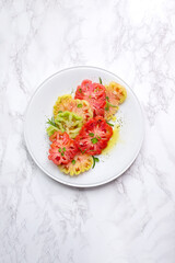 Red, green and yellow tomato slices on white plate.