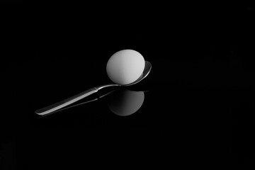 An egg on a spoon. With reflection on a black background