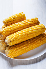 Boiled corn close up. Cobs of boiled corn on a plate. Sweet corn on the table. Cobs of sweet juicy corn. Grain background with free space. Vegetarian food. Cereal culture.