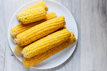 Boiled corn close up. Cobs of sweet juicy corn. Cobs of boiled corn on a plate. Sweet corn on the table. Grain background with free space. Vegetarian food. Cereal culture.
