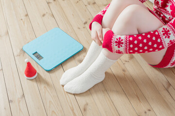 Female feet near  blue electronic scales for weight control  with Christmas santa hat on wooden floor