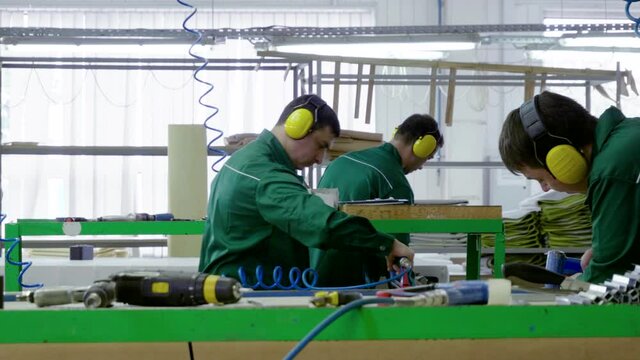 Workers dressed in uniform make a sofa, couch or settee in a furniture factory. 4K