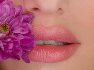 Cosmetics, makeup and trends. Bright lip gloss and lipstick on lips. Closeup of beautiful female mouth with natural lip makeup. Beautiful part of face. Perfect clean skin, whith teeth and flowers