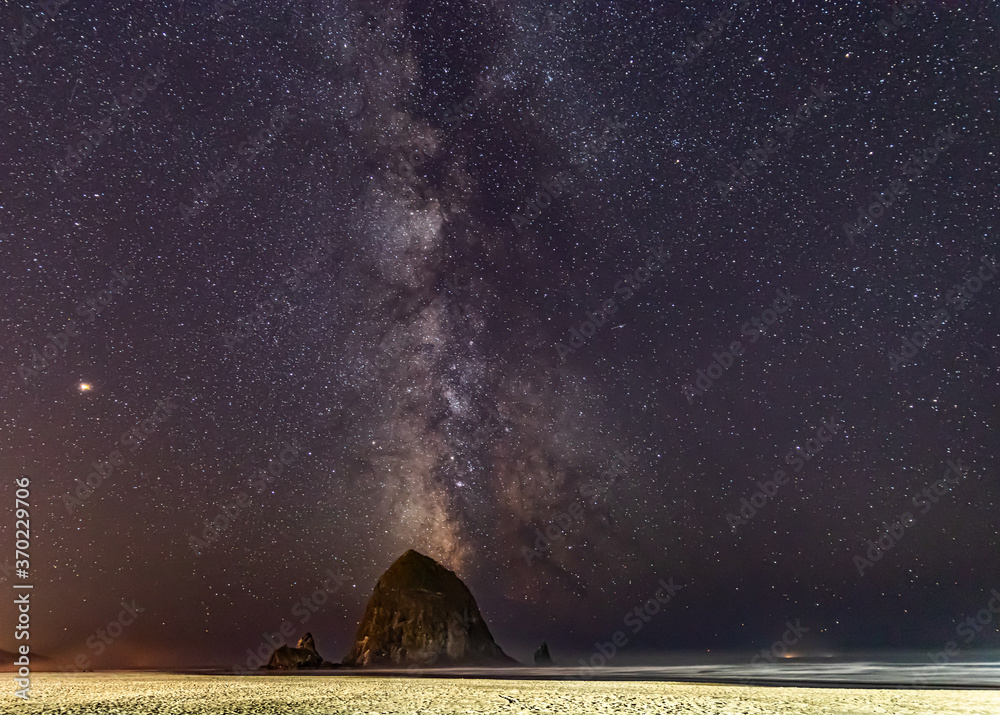 Wall mural milky way shines in the sky behind haystack rock on cannon beach in oregon