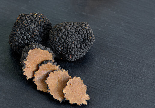Black truffles and slices on black stone background