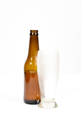 Brown glass bottle and a cold empty glass on a white background.