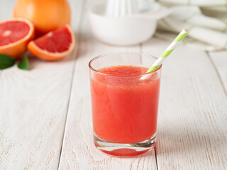 Glass of freshly squeezed grapefruit juice with pulp and drinking straw on a white wooden table. Vegetarian, raw food diet and healthy eating.