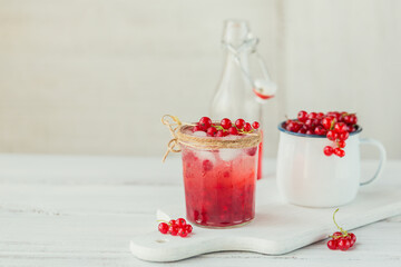 Glass of red currant cocktail or mocktail, refreshing summer drink with crushed ice and sparkling water on a white wooden background.
