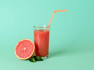 Glass of freshly squeezed grapefruit juice with pulp, drinking straw and half of grapefruit on a mint green background. Vegetarian, raw food diet and healthy eating.