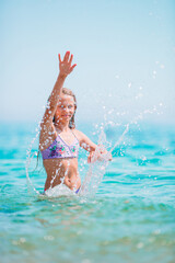 Happy child splashing in the waves during summer vacation on tropical beach. Girl play at the sea.