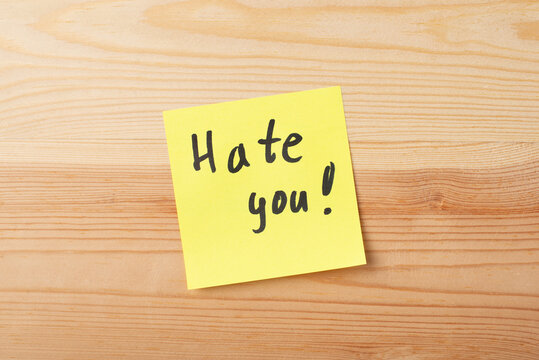 Close-up picture of yellow paper on a wooden board with inscription HATE YOU! Concept of hate, hesitation, dislike, regret