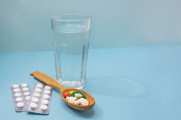 Lot of pills in spoon and glass of water on blue background. Medical concept. Excessive drug use....